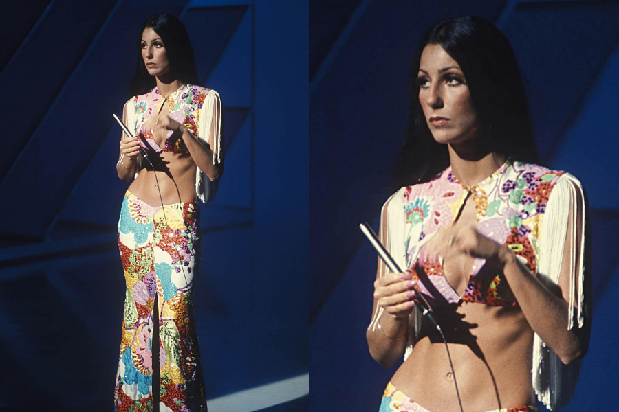 Woman on stage in a bold 70s ensemble with a fringed crop top and colorful floral bell-bottom pants, holding cue cards with long dark hair flowing. Second image shows her focused expression under stage lighting.