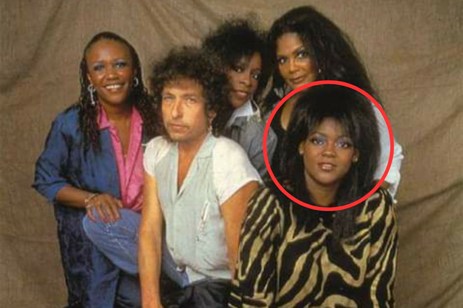 Bob Dylan sitting among four women, all smiling, in a posed group photo with one woman in front circled in red.