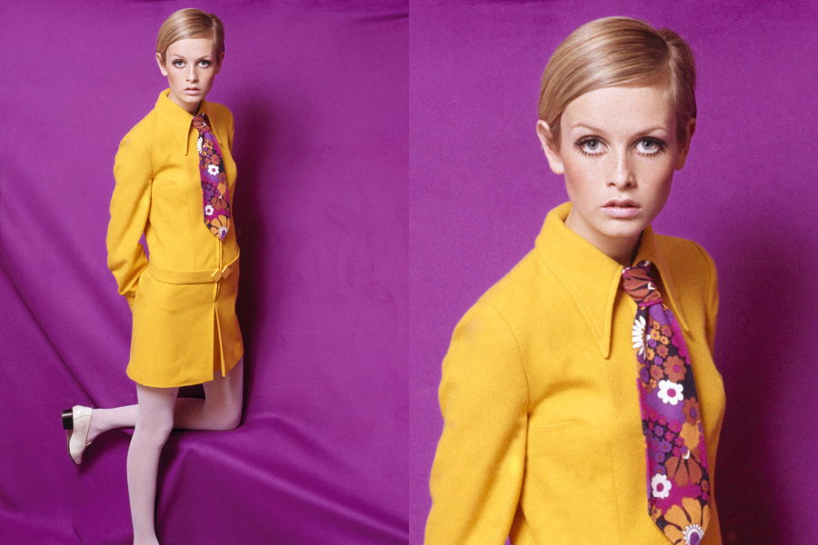 Model wearing a bright yellow skirt suit with a bold floral tie poses in front of a deep purple backdrop. Second image zooms in on her iconic short hair and wide-eyed expression.