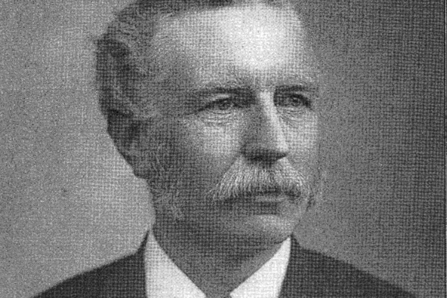 Black-and-white portrait of an elderly man with a full mustache and side-parted hair, dressed in a formal suit and white shirt.