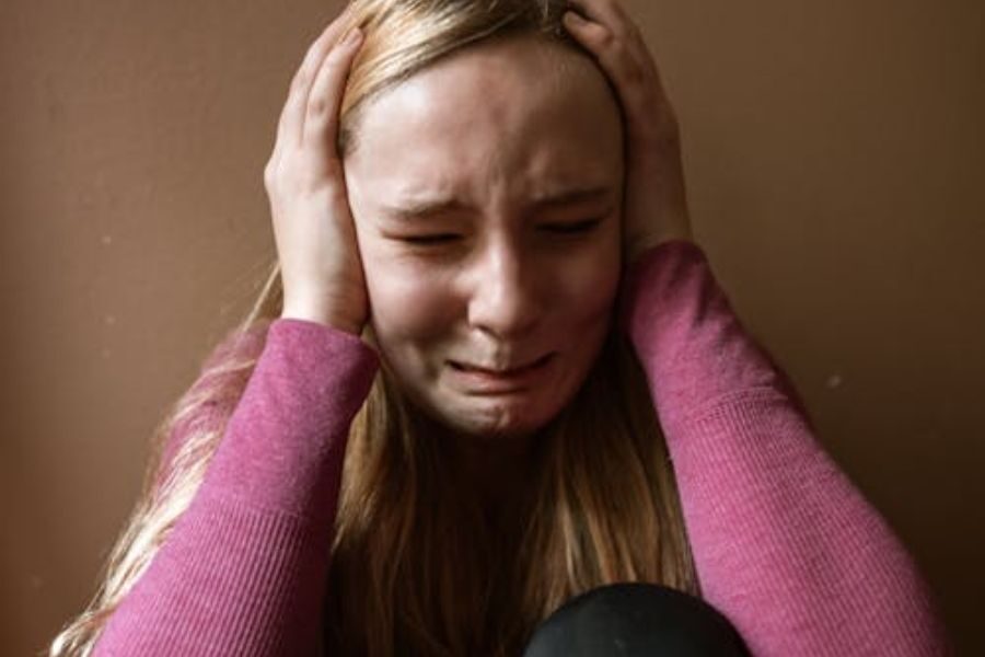 Close-up of a young girl crying with her hands covering her ears, showing visible distress.