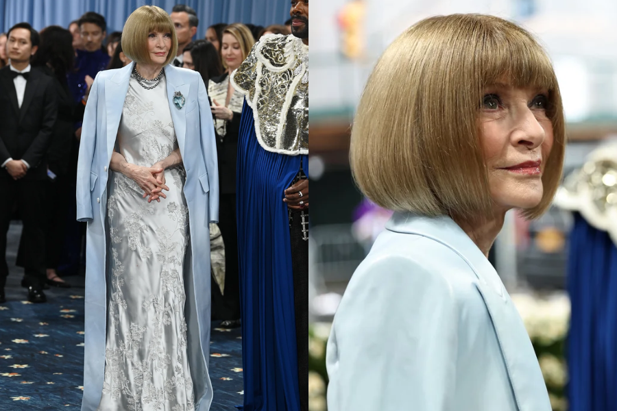 Woman in a long powder-blue coat over an embroidered silver gown standing confidently among a crowd. Close-up image highlights her precise bob haircut and soft makeup.
