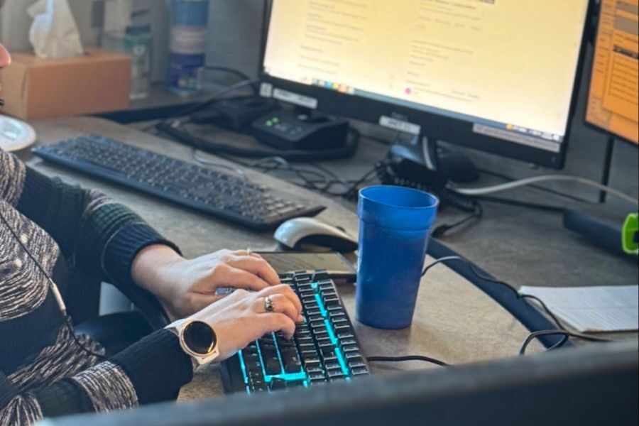 Woman typing at a computer workstation with dual monitors and a blue plastic cup on the desk.