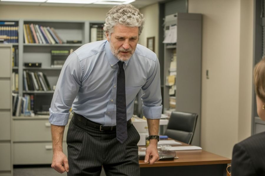 A man in a dress shirt and tie leans forward with a stern expression, speaking forcefully to someone off-frame in an office.