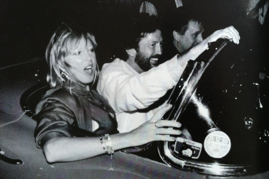 Pattie Boyd and Eric Clapton laugh and gesture while sitting in a convertible at night, likely leaving an event.
