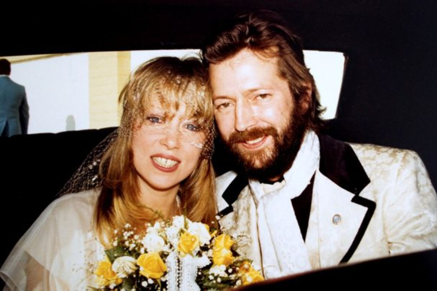 Wedding day portrait of Pattie Boyd and Eric Clapton smiling inside a car, with Boyd holding a yellow and white bouquet.