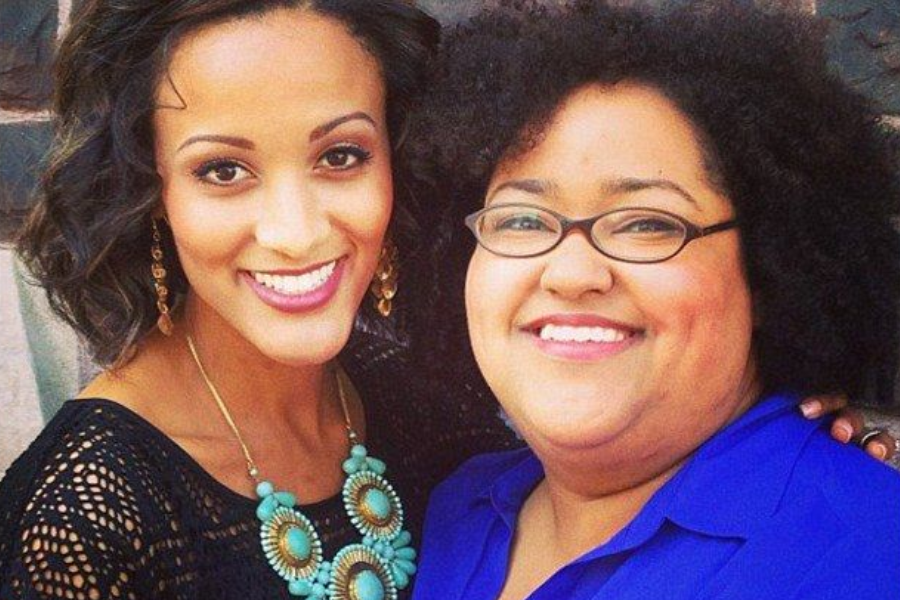 Two women smiling warmly for the camera, one wearing a bold turquoise necklace and the other in glasses and a blue blouse.
