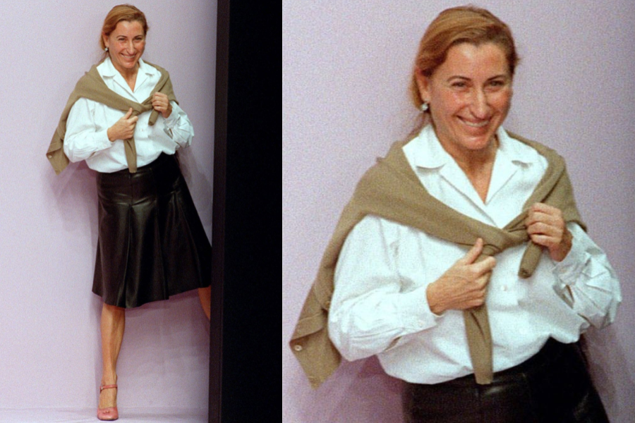 Woman smiling while standing in a white button-up shirt tucked into a black leather skirt with a light sweater tied over her shoulders. Close-up captures her natural makeup and relaxed elegance.