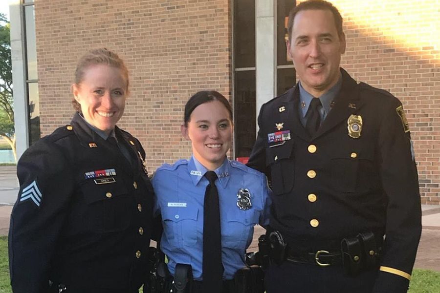 Three police officers in uniform pose smiling together outside a brick building in the evening light.