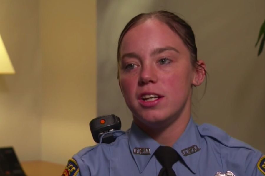Female officer in a blue uniform speaks during an interview indoors, looking slightly to the side.