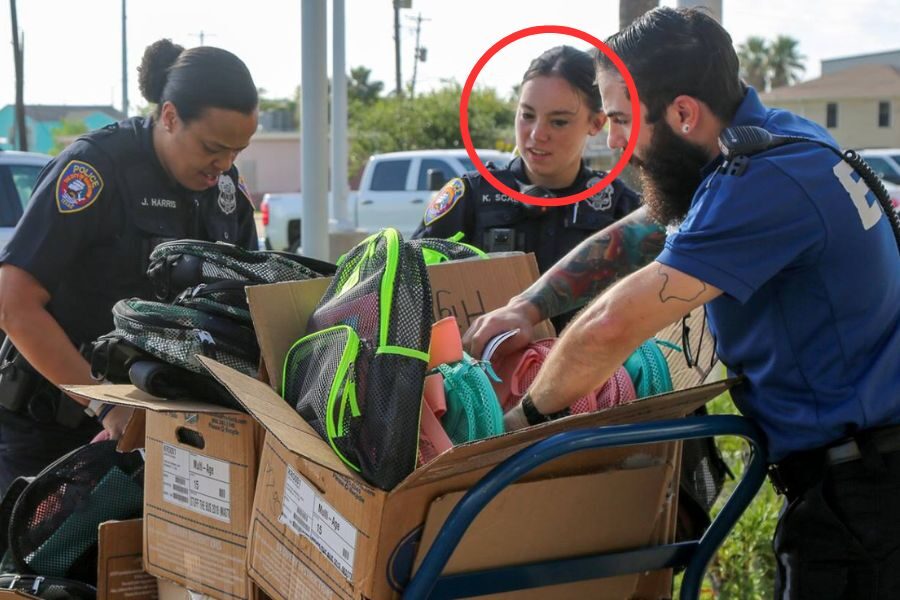 Police officers sort backpacks from large cardboard boxes during a community giveaway event, with one officer circled in red.