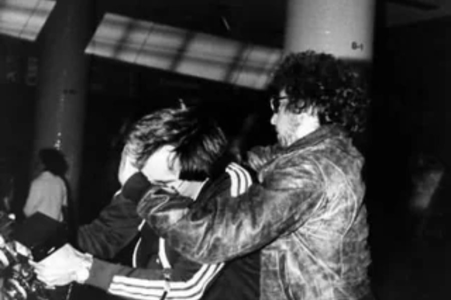 Grainy black and white image of a man grabbing another man by the head in what appears to be a chaotic or possibly aggressive moment in a crowded space.