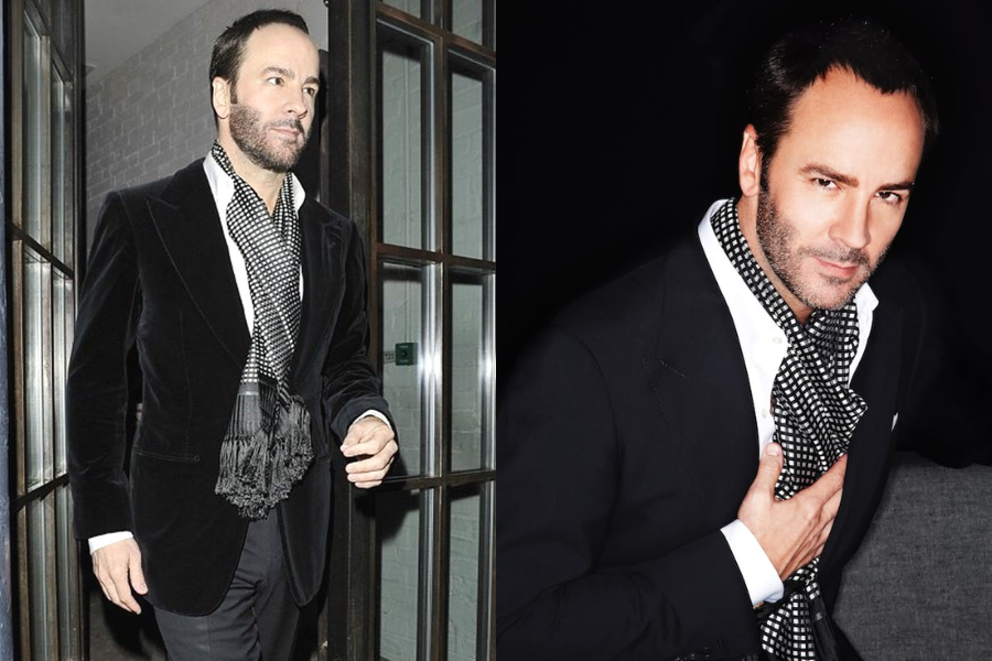 Man in a black velvet suit jacket with a checkered silk scarf tied at the neck, posing indoors with a suave demeanor. Close-up reveals his tailored grooming and sharply styled beard.