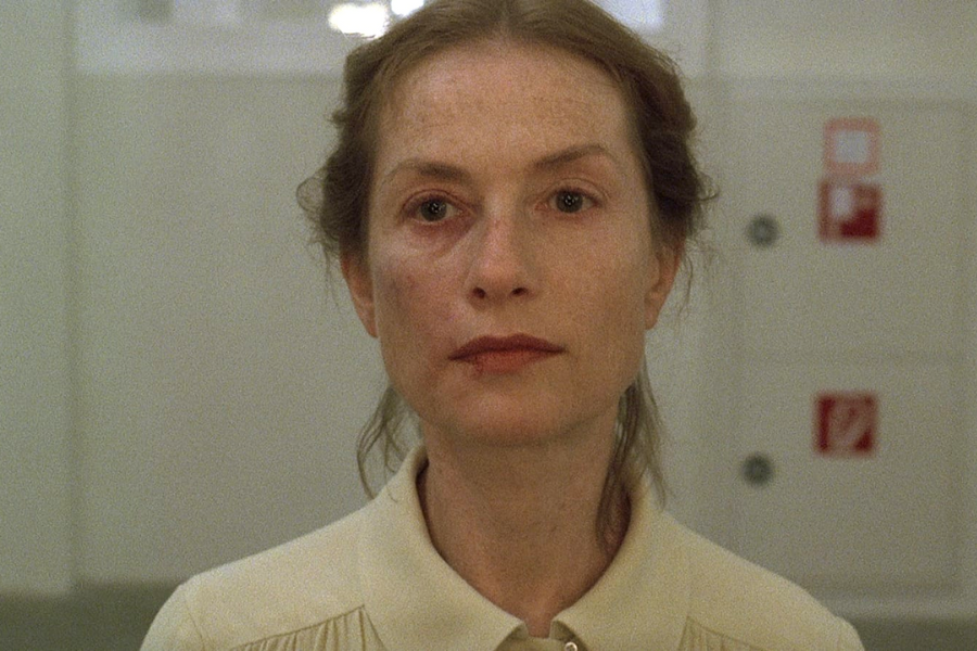 A woman with red-rimmed eyes and a cut on her lip stares straight ahead with an emotionless expression in a sterile white room.