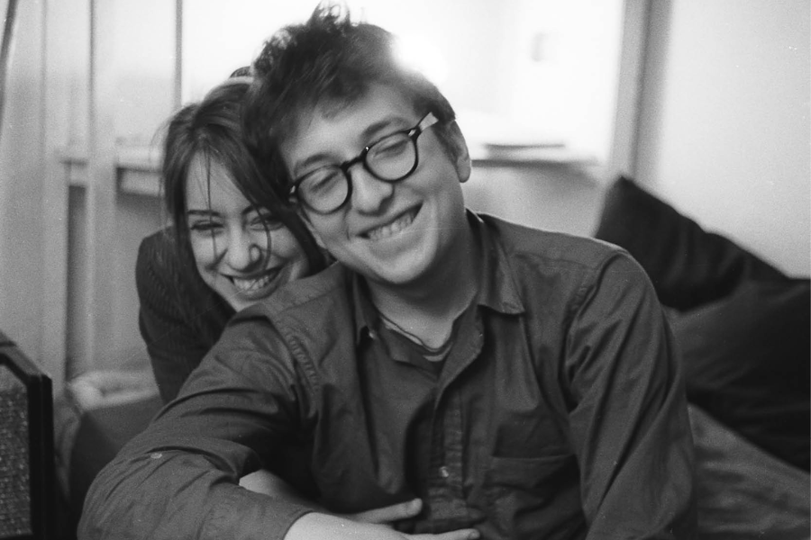Black and white photo of a young couple smiling and leaning closely together indoors, radiating warmth and intimacy.