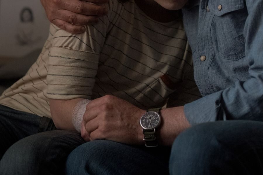 A comforting moment between an adult and a child, with the adult’s arm around the child who has a bandage on their forearm.