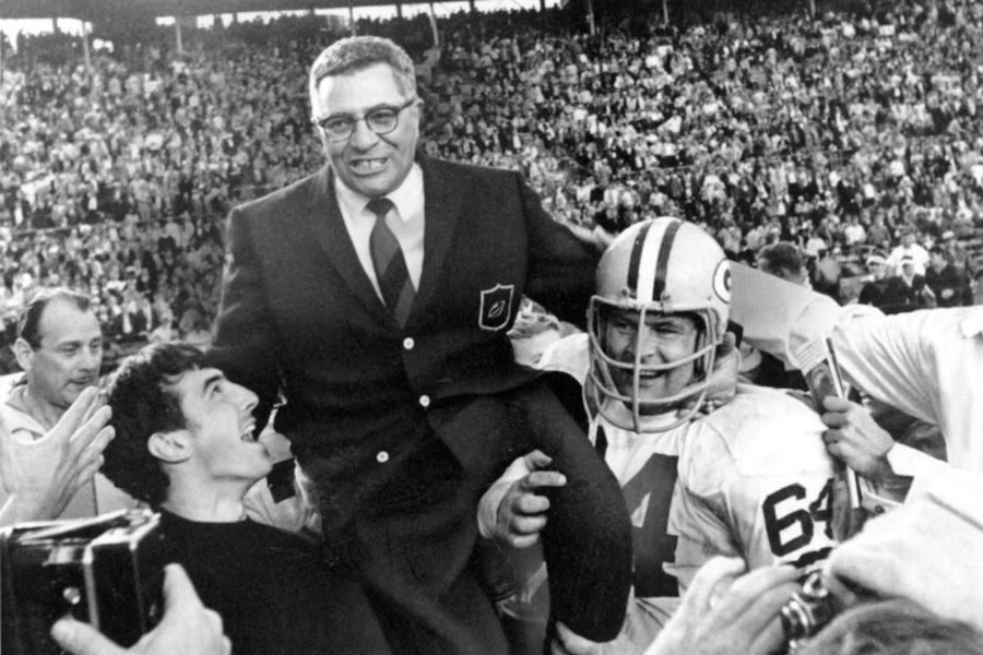 A triumphant scene with a bespectacled man in a suit being lifted by football players in a crowded stadium, exuding joy and celebration.