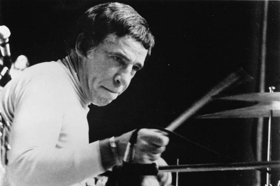 Black and white image of a focused drummer playing energetically on stage. The motion blur of the drumsticks conveys dynamic movement and intensity.
