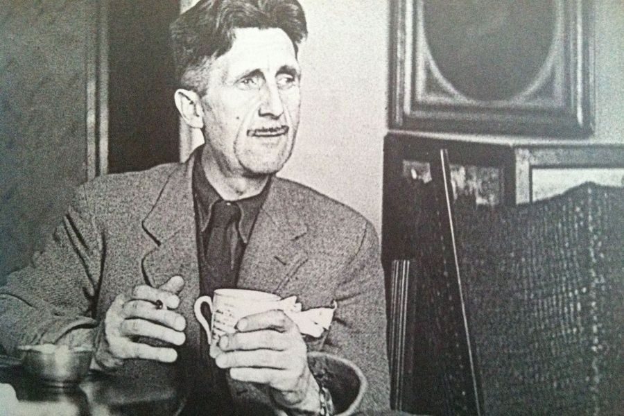 Black-and-white portrait of a man in a suit, holding a cup and a cigarette. He appears thoughtful, with a vintage-inspired room in the background.