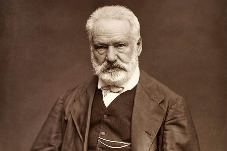 Sepia-toned portrait of an elderly man with a white beard and serious expression, wearing a suit and bow tie, set against a plain background.