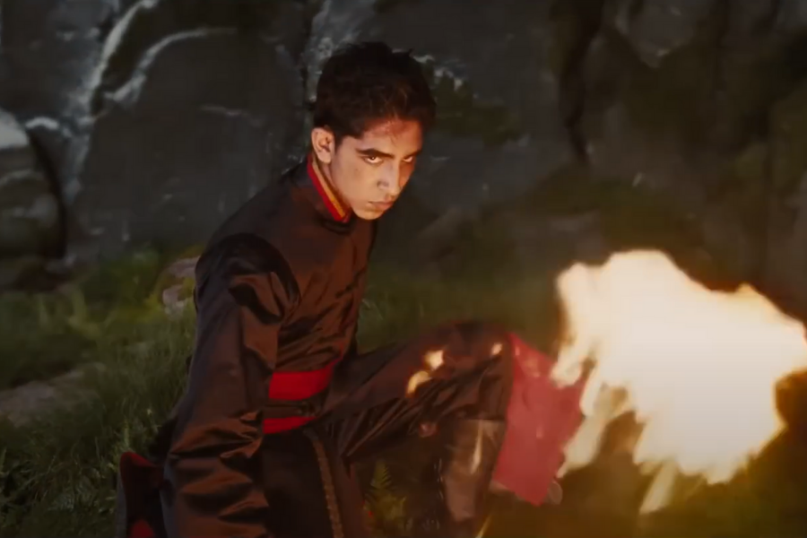 A young man in a dark outfit and red sash crouches with an intense gaze, conjuring flames from his fist. The rocky, dimly lit background adds drama.