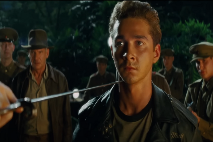 A tense scene showing a young man in a leather jacket looking intently at a sword pointed at him, surrounded by soldiers in hats, conveying suspense.