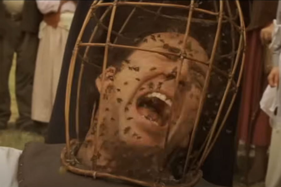 A person in distress is trapped in a wicker cage covering their head, filled with bees. The scene conveys fear and panic with onlookers in the background.