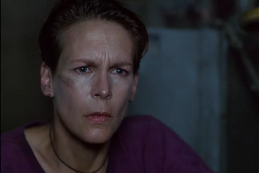 A person with a concerned expression looks intensely forward. They have short hair and wear a dark shirt. The background is dim, adding a tense atmosphere.