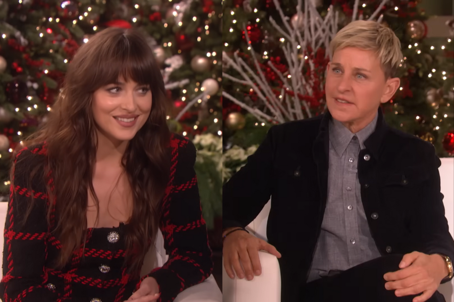 Two people sit on a talk show set decorated for the holidays. They are talking and smiling, with festive trees and lights in the background.
