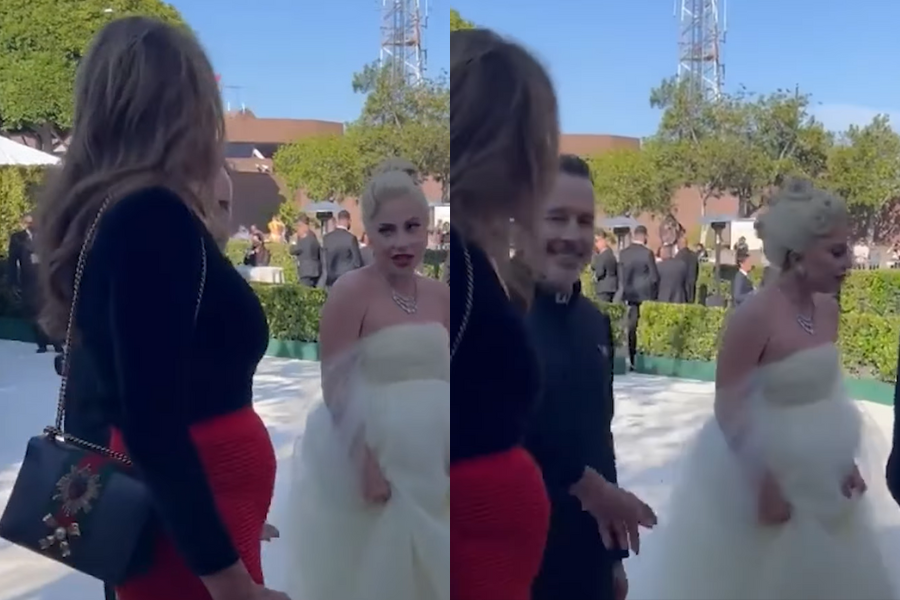 Outdoor event with elegantly dressed people. A woman in a white gown walks past a woman in red and black, engaging in friendly conversation. Lively ambiance.