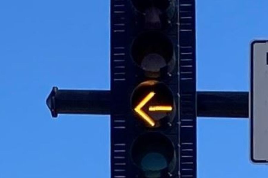 Yellow left turn arrow illuminated on a traffic light against a clear blue sky.