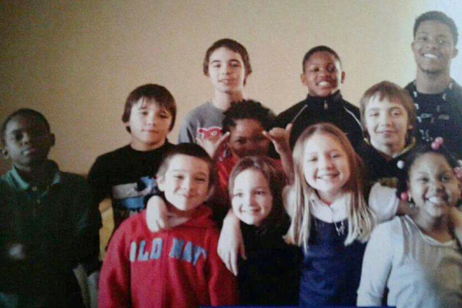 A group of twelve smiling children posing for a photo indoors, wearing casual clothing with friendly expressions.