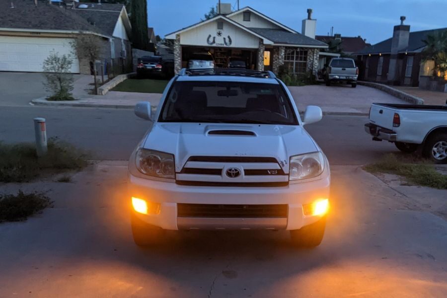 White Toyota SUV with headlights on, parked in a residential driveway during early evening.