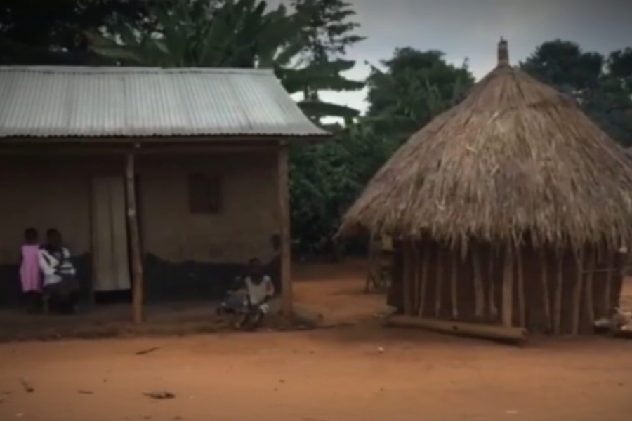A rural homestead with a traditional thatched hut and a simple building with children standing nearby.