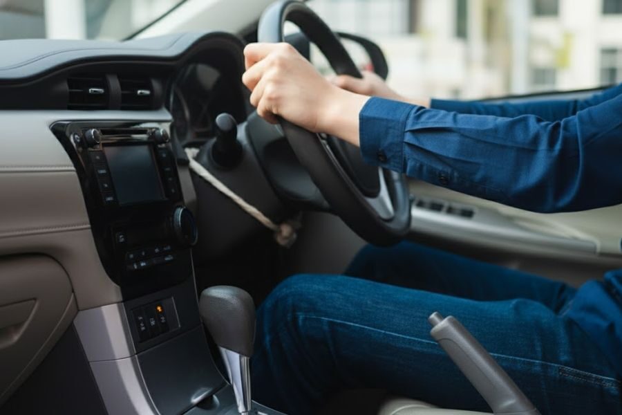 Person in blue long-sleeve shirt holding a steering wheel while driving a car.