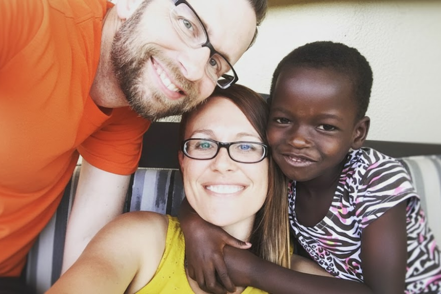 A smiling couple takes a selfie with a young girl between them, all appearing happy and close together.