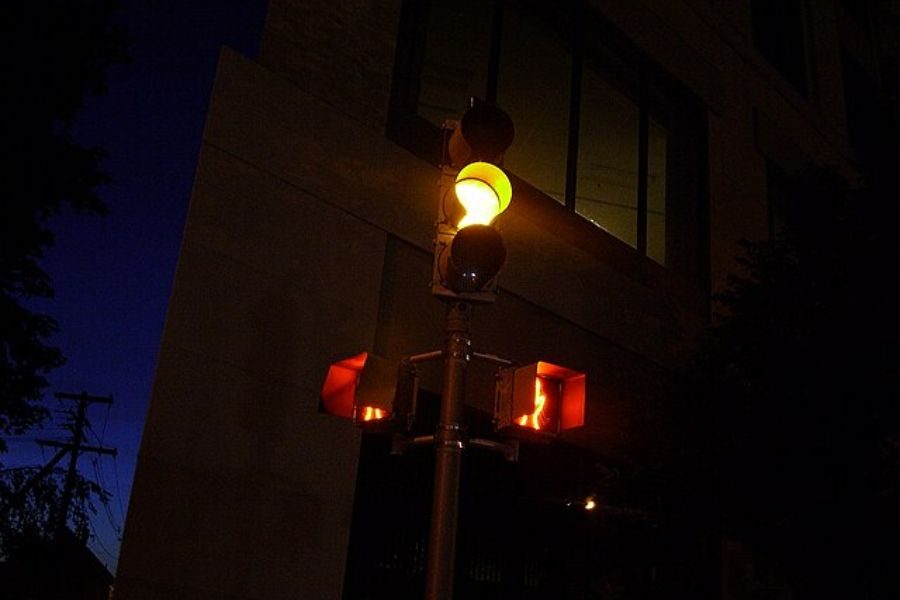 Yellow traffic light glowing at night on a city street corner with a pedestrian crossing signal also visible.