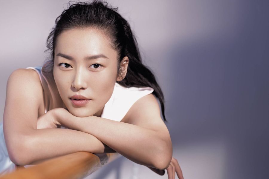A model leans on a ballet barre in soft lighting, wearing a minimalist white top with a clean and natural makeup look.