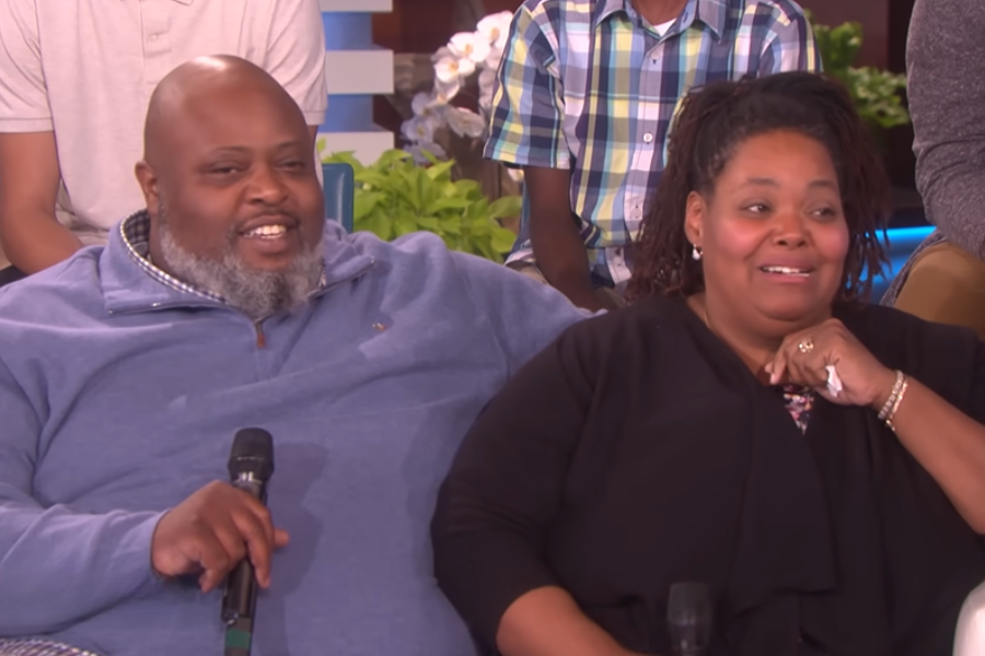 A close-up of a man and woman smiling and sitting together on a white couch, each holding a microphone.