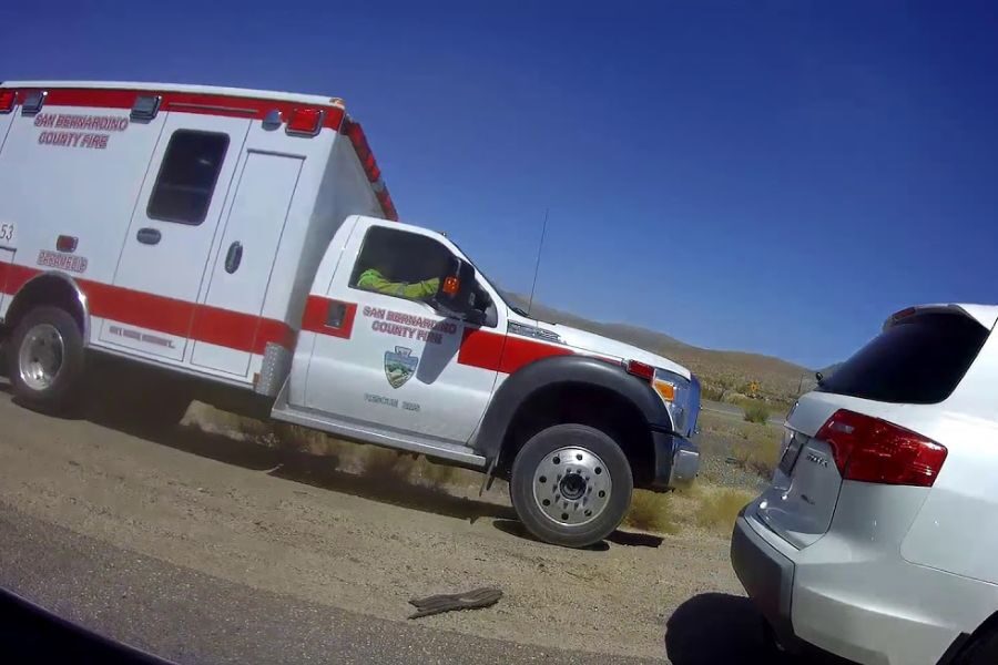 San Bernardino County Fire emergency vehicle parked beside a white SUV on the shoulder of a desert road.