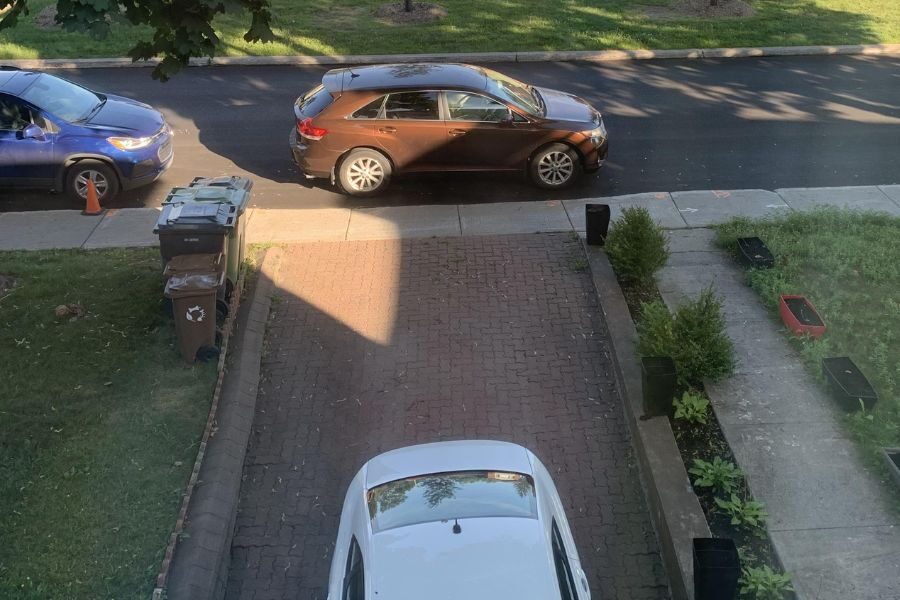 View from a house above a driveway with a white car parked in the driveway and two other cars on the street.