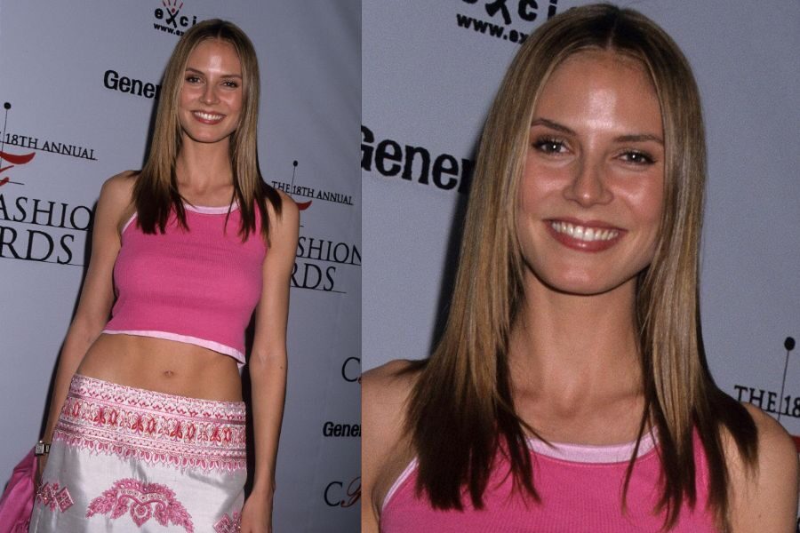 A smiling model in a pink tank top and patterned skirt poses on the red carpet at a fashion awards event.