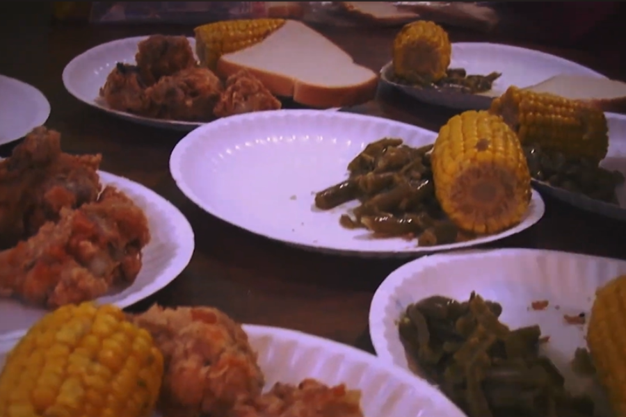 Paper plates filled with fried chicken, green beans, corn on the cob, and bread laid out on a table.