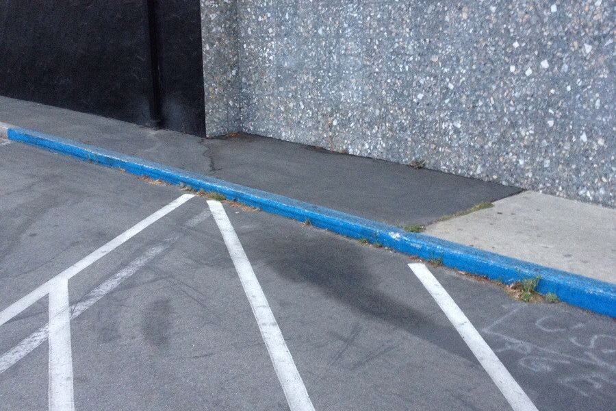 Blue-painted curb next to a sidewalk and a marked parking lot, possibly indicating a restricted parking area.