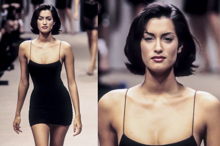 A runway model in a fitted black mini dress walks confidently with a close-up showing bold features and sleek bob haircut.