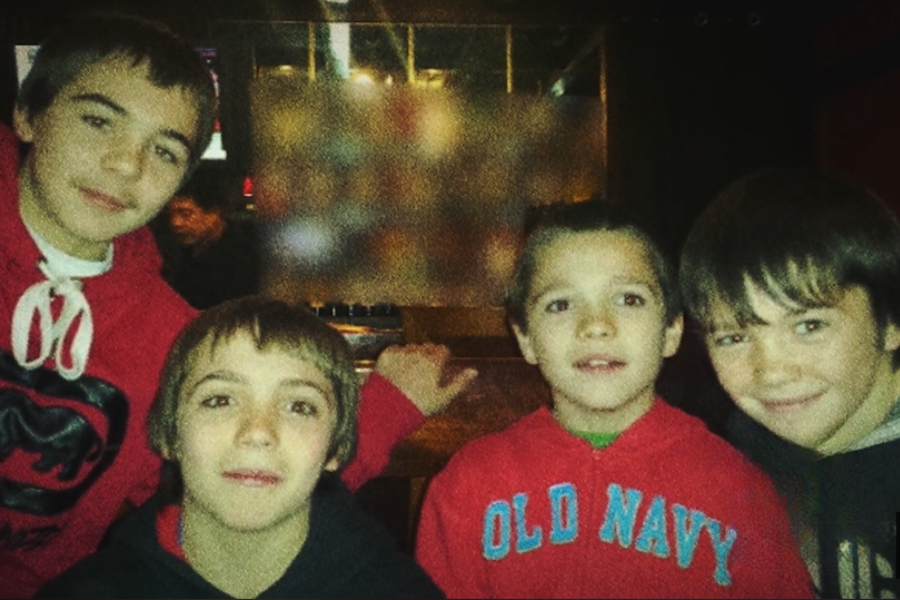Four boys in casual hoodies posing together in a dimly lit room, with one wearing an "Old Navy" sweatshirt.