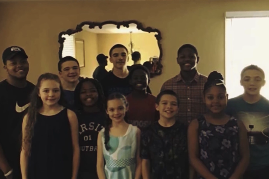 A group of smiling children posing indoors in front of a decorative mirror, with natural light shining from the side.