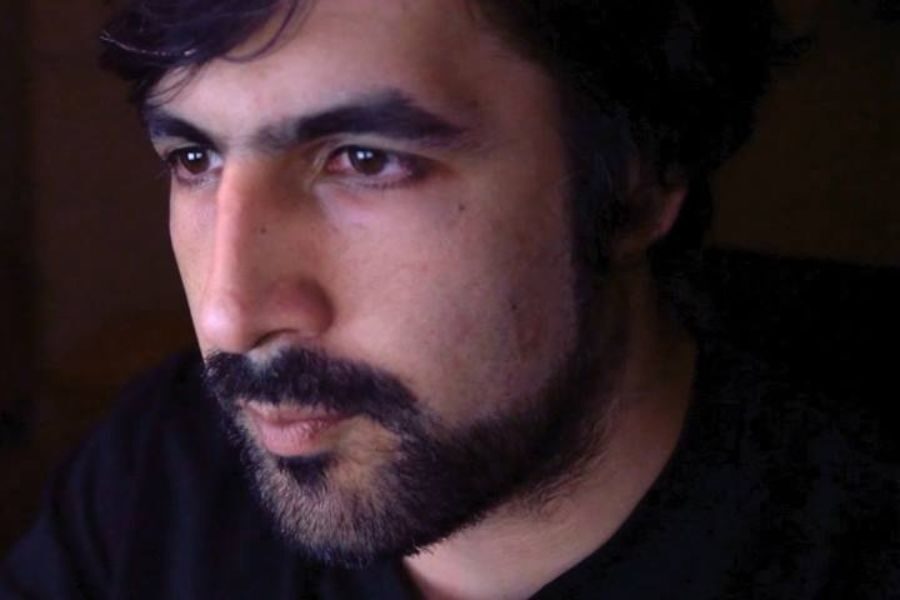 Close-up of a man with dark hair and a beard staring intently at a screen in a dimly lit environment.