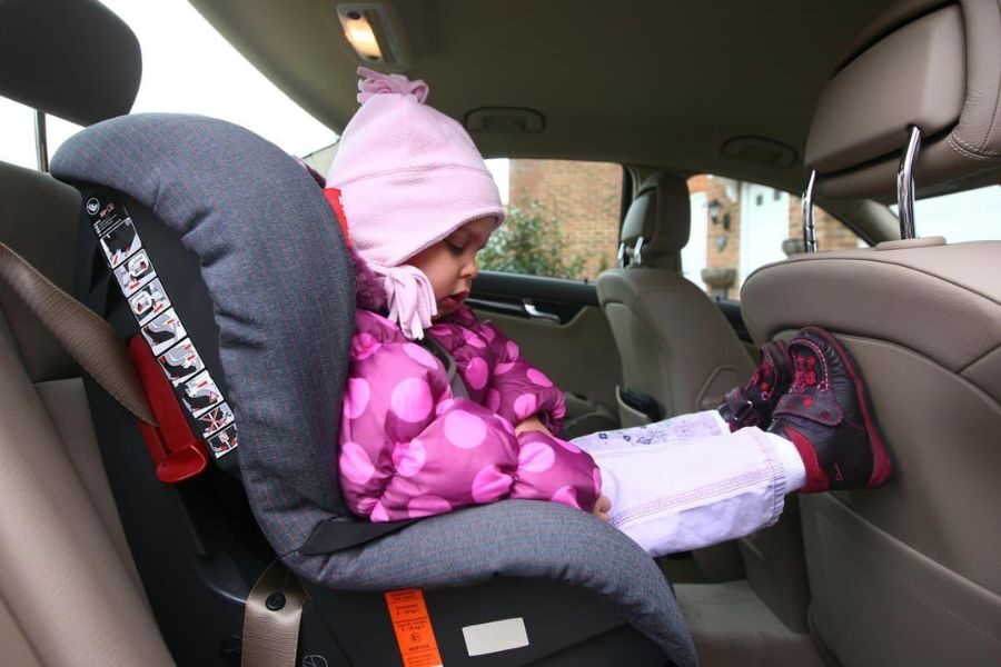 Young child in a rear-facing car seat dressed in a pink coat and hat, sitting in the backseat of a car.