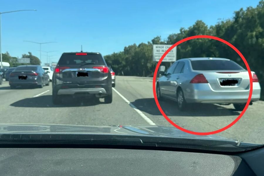 Silver car circled in red driving on the shoulder of a highway to bypass traffic congestion.
